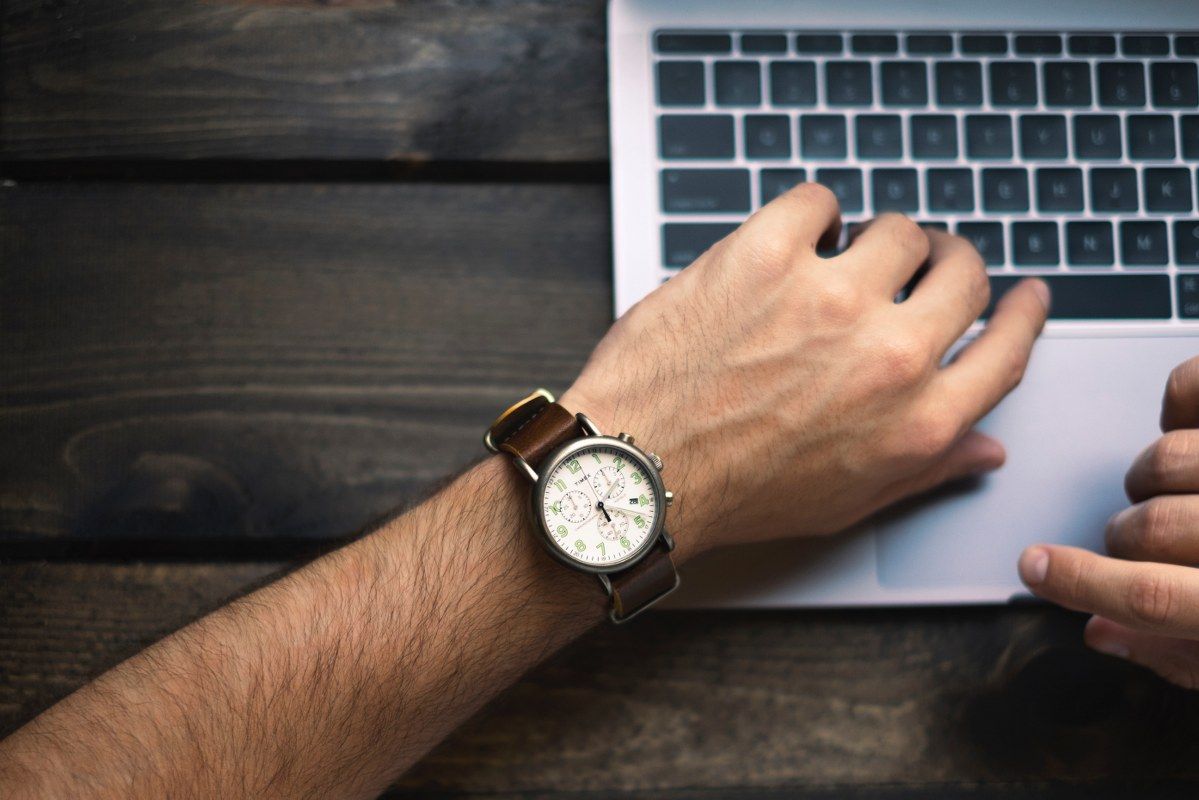 Een man met een horloge om zijn pols achter de laptop voor digitaal factureren